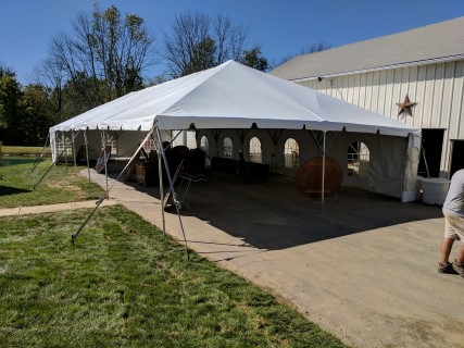 Wedding Reception - 30' x 75' Frame Tent (Free Span) on Driveway, Cathedral Sidewalls, Wood Chairs, Round Tables, Rectangular Head Tables. Anchored on One Side with Water Barrels.